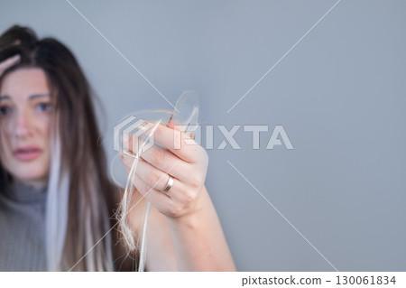 Young woman showing effects of severe hair loss after brushing strands in beauty or hair care context 130061834