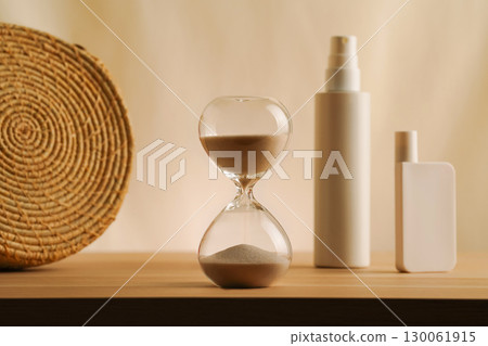 Elegant arrangement of an hourglass, and cosmetic spf bottles on a simple beige backdrop. Lowkey natural concept of summer luxury skincare and protection, warm tone minimalist muted photo 130061915
