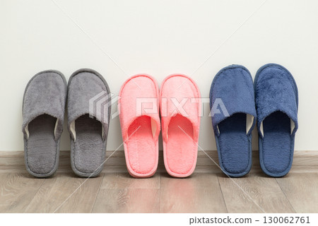 Three pairs of home slippers near the white wall. Shoes for home usage concept Three pairs of home slippers near the white wall. Shoes for home usage concept 130062761
