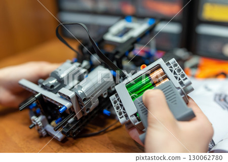 Mechanism made of electric engineering constructor, focus on power block with accumulators in it. Child playing with technological toy, building robot machine Mechanism made of electric engineering constructor, focus on power block with accumulators in it. Child playing with technological toy, building robot machine 130062780