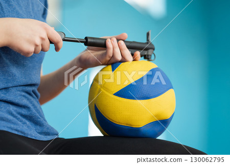 Close up of girl inflating volleyball ball on indoor court before training. Old ball deflates with time 130062795