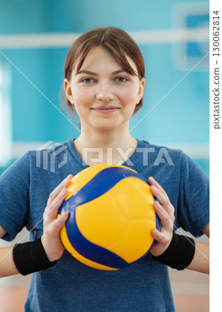 Portrait of a young girl with volleyball. Happy female volleyball player with new professional ball in gym Portrait of a young girl with volleyball. Happy female volleyball player with new professional ball in gym 130062814