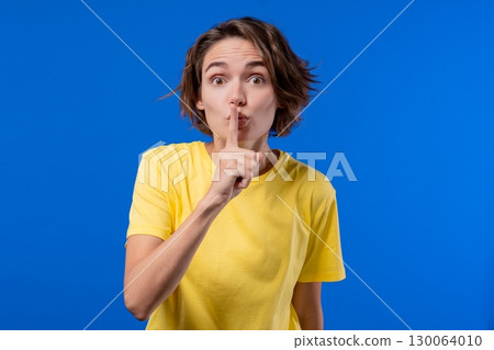 Beautiful woman makes shush shh gesture with finger on lips, silence signaling 130064010