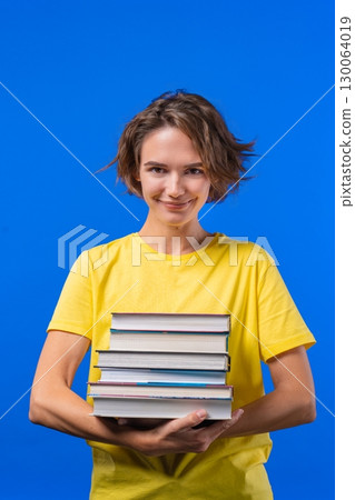 Happy Student Woman With Stack Books From Library, Blue Background. girl smiles 130064019