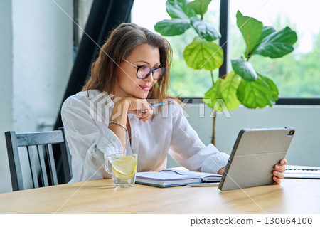 Middle aged female teacher entrepreneur using digital tablet for video online meeting 130064100