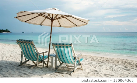 Scenic tropical beach with two colorful striped deck chairs under a large parasol 130064363