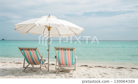 Scenic tropical beach with two colorful striped deck chairs under a large parasol 130064389
