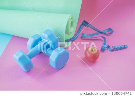 Fitness concept with dumbbells, measuring tape on bright background. Blue dumbbells and yoga mat on gradient surface. Fitness concept with dumbbells, measuring tape on bright background. Blue dumbbells and yoga mat on gradient surface. 130064741