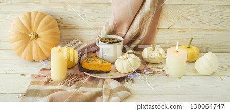 Autumn still life with pumpkin pie, cup of coffee and various decorative pumpkins against a wooden surface and a warm blanket. 130064747