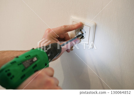 Person uses a power screwdriver to install electrical outlet cover plate on white wall. Home repair, DIY projects, electrical work and professional craftsmanship Person uses a power screwdriver to install electrical outlet cover plate on white wall. Home repair, DIY projects, electrical work and professional craftsmanship 130064852