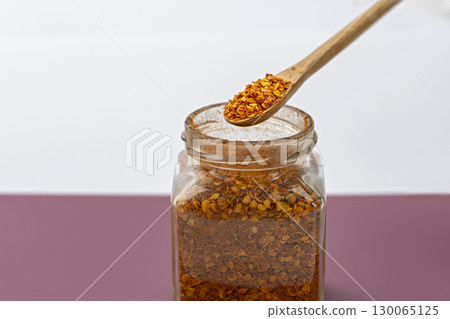 Wooden spoon with chili flakes above glass jar spicy seasoning dried red pepper kitchen ingredient aromatic culinary flavor enhancer food preparation 130065125
