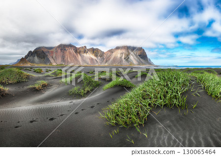 Astonishing sunny day and gorgeous rippled black sand beach with dunes and green grass on Stokksnes cape in Iceland. Astonishing sunny day and gorgeous rippled black sand beach with dunes and green grass on Stokksnes cape in Iceland. 130065464