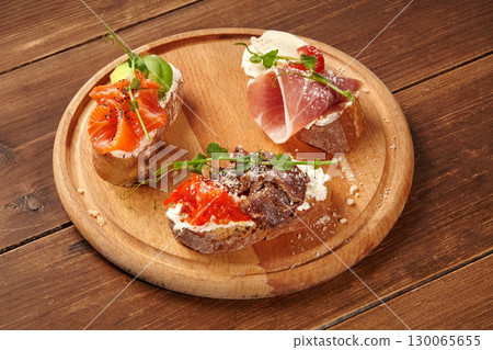 Delicious bruschetta with salmon, prosciutto, and roast beef resting on wooden board 130065655