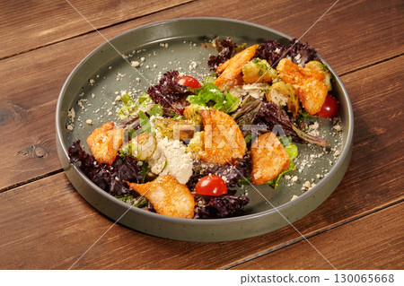 Delicious caesar salad with chicken, croutons, parmesan, and cherry tomatoes on rustic wooden table 130065668