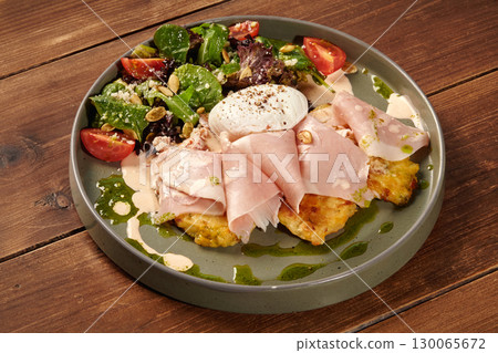 Potato pancakes with ham, poached egg and salad on wooden table 130065672