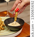 Woman dipping fried vegetables in a creamy sauce with a glass of white wine 130065692