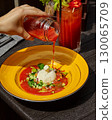 Chef pouring gazpacho over burrata cheese and chopped vegetables 130065709