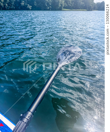 Close-up of a paddle over blue rippling lake water with forest in the background, symbolizing adventure, kayaking, and outdoor activities. High quality photo 130066214