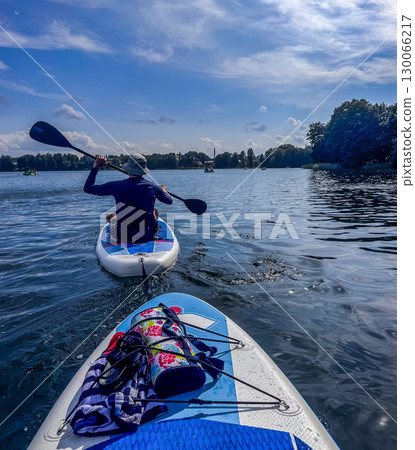 Person enjoying paddle boarding on a bright summer day with calm water and scenic forest view. High quality photo 130066217