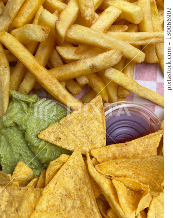 Golden crispy tortilla chips with creamy guacamole and french fries appetizer platter 130066902