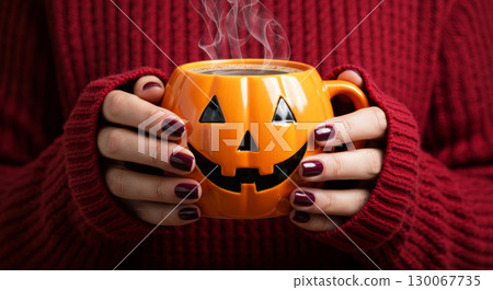 Hands in red sweater holding steaming Jack-o'-lantern mug. Cozy Halloween atmosphere. Hands in red sweater holding steaming Jack-o'-lantern mug. Cozy Halloween atmosphere. 130067735