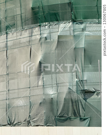 Green mesh netting covering construction scaffolding, abstract urban texture, modern protective fabric wrap on building renovation site in strong daylight Green mesh netting covering construction scaffolding, abstract urban texture, modern protective fabric wrap on building renovation site in strong daylight 130067805