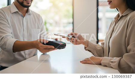 Contactless payment with smartphone and card reader, smiling man and woman at counter 130069387