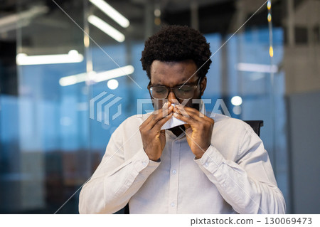 Professional setting depicts individual sneezing due to illnesses like a cold or allergy. Depicts health concerns and workplace well-being. 130069473
