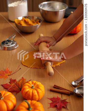 child rolls out dough surrounded by autumn elements like pumpkins, leaves, and cinnamon 130069476