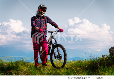 Unrecognizable athlete in protective gear standing in a field and looking at the camera against the backdrop of foggy mountains and cumulus clouds. Mountain sports concept 130069990