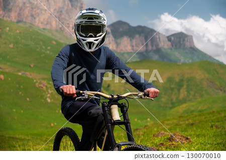 Male athlete cyclist in helmet and protective mask outdoors. MTB rider in mountainous terrain against the backdrop of epic rocks. Male athlete cyclist in helmet and protective mask outdoors. MTB rider in mountainous terrain against the backdrop of epic rocks. 130070010