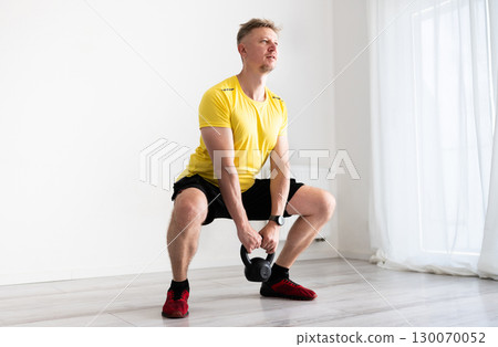 Sporty Man Doing Home Workout With Dumbbells And Squats 130070052