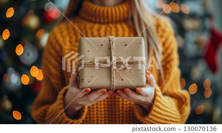 Close-up of a woman in a cozy oversized mustard yellow sweater holding wrapped Christmas present 130070136