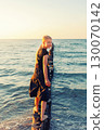 Cute adorable blond teenager happy kid girl walking by wooden breakwater posts at Baltic sea scenic warm summer sunset light. Balancing reflects challenges, choices and uncertainties of growing up 130070142