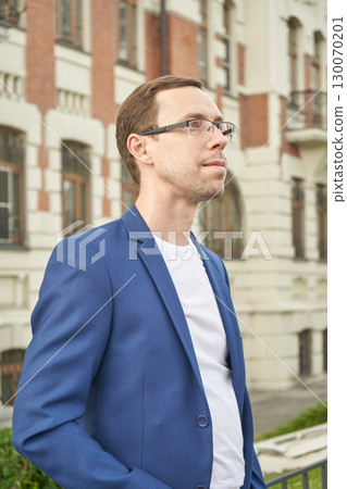 Young caucasian male in blue blazer standing outdoors by historic building 130070201