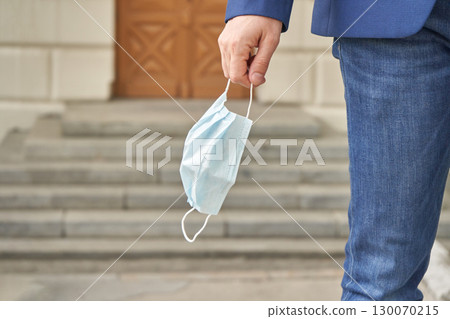 Adult male holding face mask in hand wearing blue jeans and blazer outside 130070215