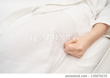 Close-up of female hand clenched in fist on white bed sheet in relaxing spa 130070235