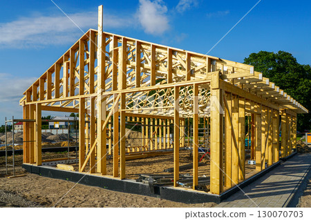 Modern wooden house frame construction with beams and roof trusses at building site under blue sky Modern wooden house frame construction with beams and roof trusses at building site under blue sky 130070703