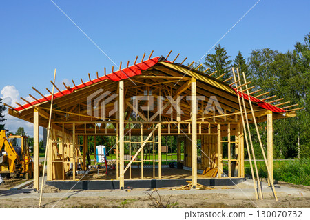 New modern wooden house under construction with visible frame, roof beams, and scaffolding support 130070732
