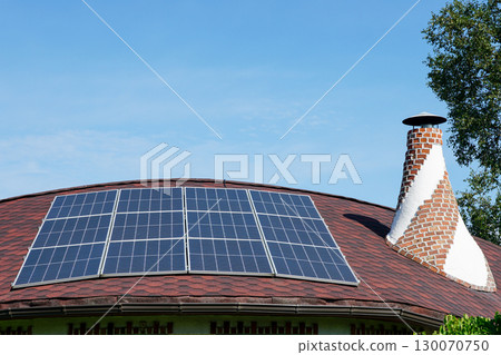 Solar panels installed on a curved red roof with chimney under blue sky, renewable energy concept 130070750