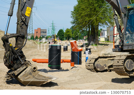 Excavator at road construction site with drainage pipes and utility installation works in progress Excavator at road construction site with drainage pipes and utility installation works in progress 130070753