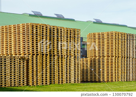 Large stacks of new wooden pallets stored outside an industrial warehouse with green roof 130070792