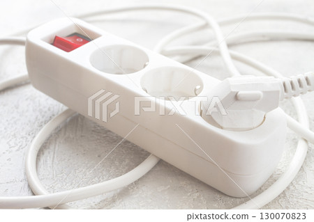 Power strip with multiple sockets and a switch in a cluttered setup on a textured surface during daytime 130070823