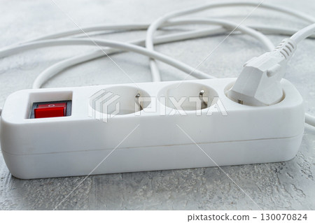 Power strip with multiple sockets and a switch in a cluttered setup on a textured surface during daytime Power strip with multiple sockets and a switch in a cluttered setup on a textured surface during daytime 130070824
