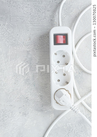 Power strip with multiple sockets and a switch in a cluttered setup on a textured surface during daytime 130070825