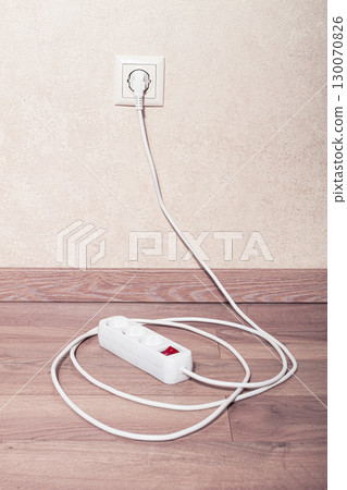 Electrical power strip connected to wall outlet on wooden floor in bright room Electrical power strip connected to wall outlet on wooden floor in bright room 130070826