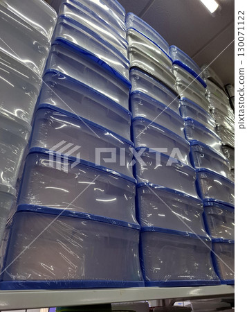 Stacks of plastic storage containers are neatly arranged on supermarket shelves, showcasing their clear design and multifunctional use for home organization. 130071122