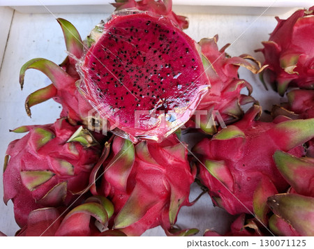 Bright red pitahaya sits among other fresh fruits at a popular farmers market in Spain during the late summer season, showcasing its unique appearance and tempting texture. Bright red pitahaya sits among other fresh fruits at a popular farmers market in Spain during the late summer season, showcasing its unique appearance and tempting texture. 130071125