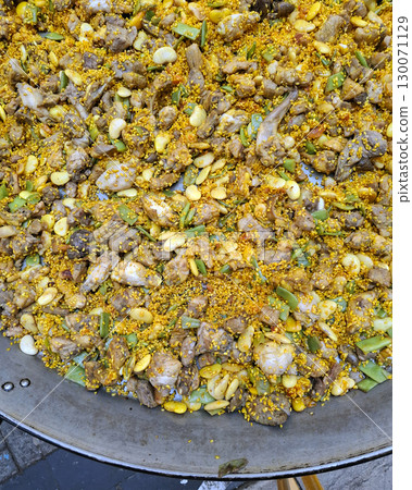 A giant frying pan is sizzling with a colorful mix of rice, tender meat, and fresh vegetables. Aromatic spices create a tempting dish, reflecting local culinary traditions during a sunny day. A giant frying pan is sizzling with a colorful mix of rice, tender meat, and fresh vegetables. Aromatic spices create a tempting dish, reflecting local culinary traditions during a sunny day. 130071129