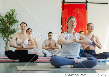 Yoga mindfulness meditation. Group of sporty people doing exercise in studio for class for yoga wellness mindfulness meditation. Men women practicing yoga sitting in lotus pose meditating relaxing 130071237